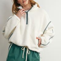 Model wearing oversized cream teddy fleece pullover with green trim and green casual shorts