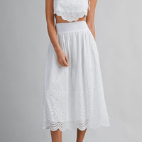 Woman wearing a white lace top and skirt set on a gray background