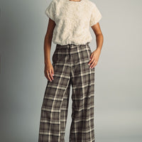 Model wearing a cream faux fur short sleeve top styled with brown plaid trousers