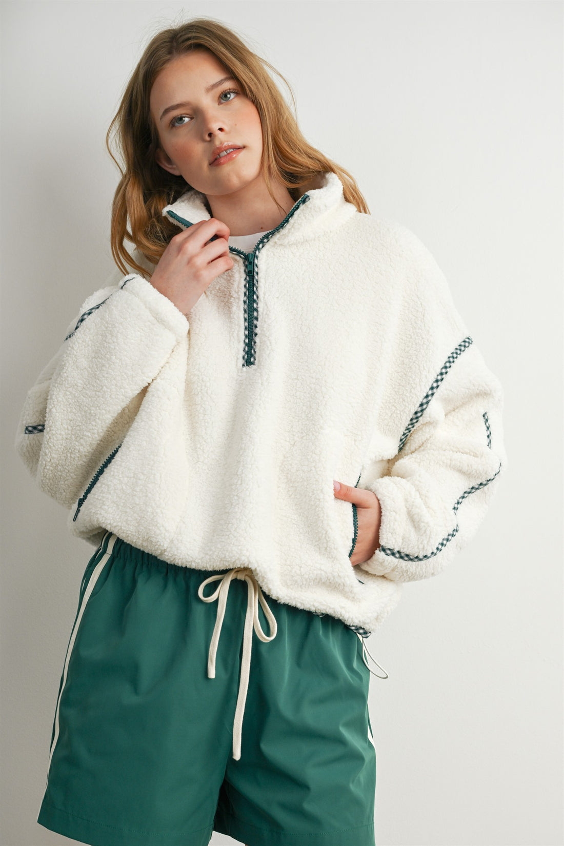 Model wearing oversized cream teddy fleece pullover with green trim and green casual shorts