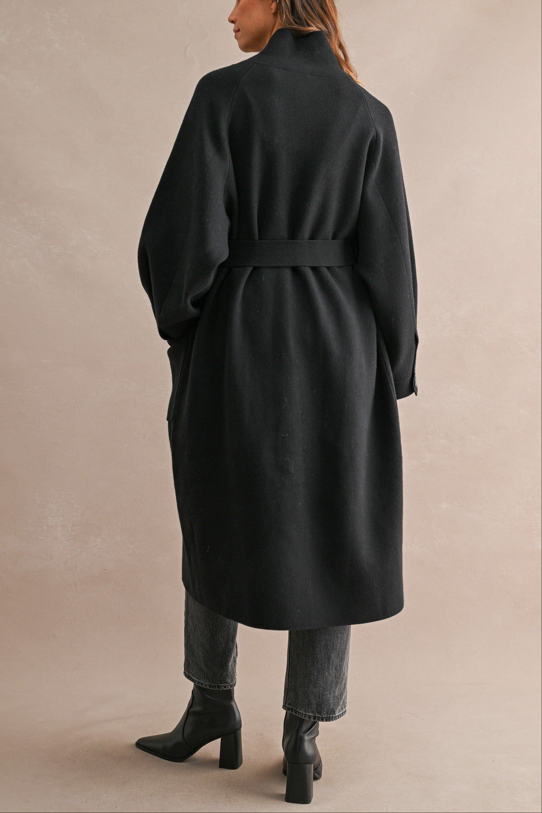 Back view of black belted long coat with relaxed silhouette and stand collar