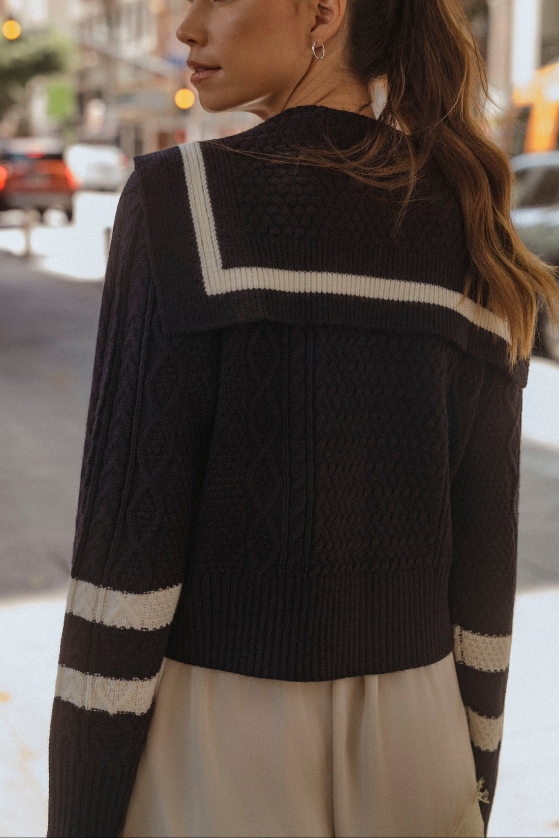 Woman wearing navy sailor collar cable knit cardigan with ivory contrast stripes and lace trim shorts