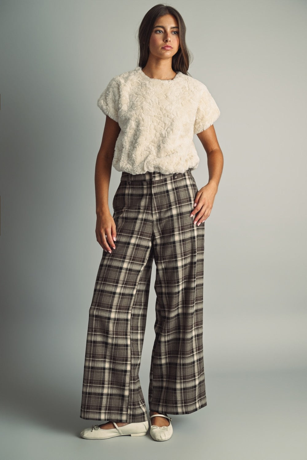 Model wearing a cream faux fur short sleeve top styled with brown plaid trousers